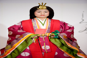 Eine Frau in einem traditionellen japanischen Kimono, das ein leuchtendes rotes und grünes Kleid mit aufwändigen Mustern trägt, steht selbstbewusst auf einem Laufsteg mit ihrem Haar zu einem ordentlichen Knoten gebunden.