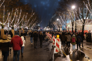 Eine Menschenmenge, die nachts eine Straße entlanggeht, mit Bäumen und Gebäuden, die von festlichen Lichtern beleuchtet sind.