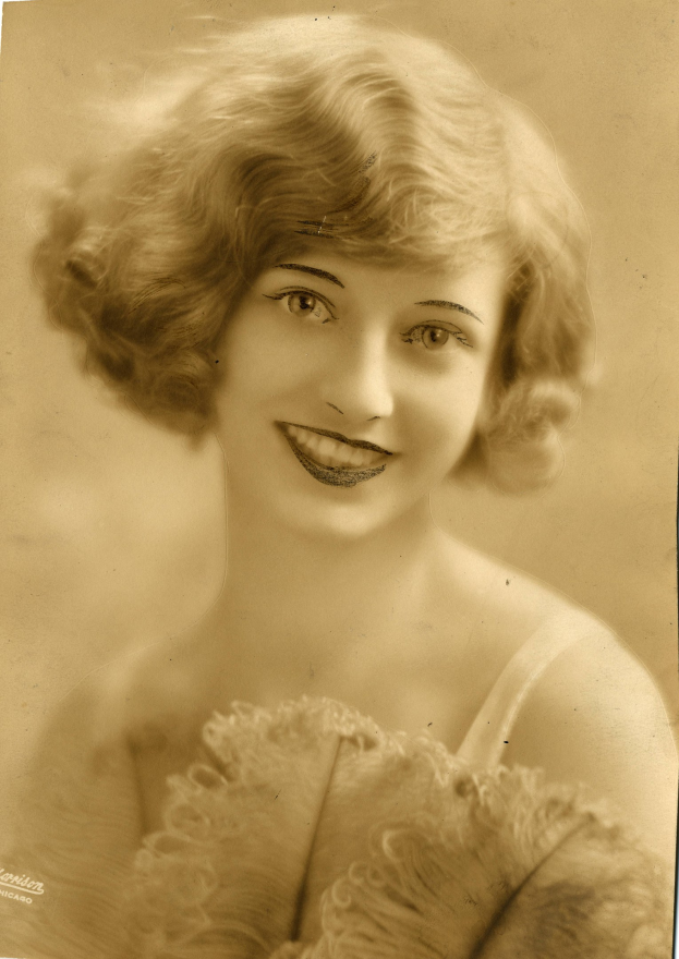 Ein Schwarz-Weiß-Foto einer Frau in einem Kleid im Stil der 1920er Jahre mit einer klassischen Frisur, die warm lächelt.