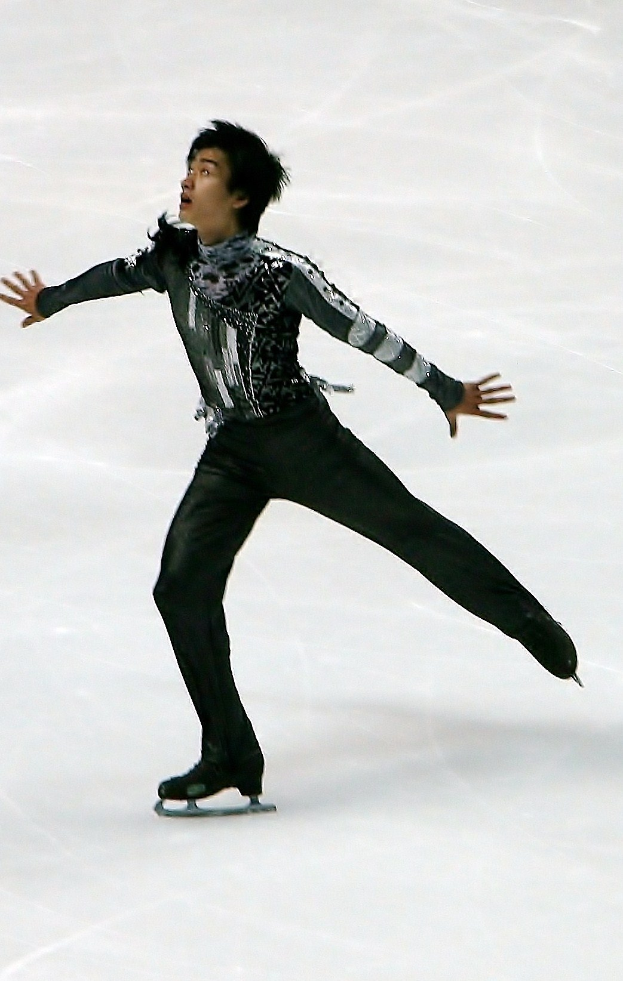 Mannlicher Eiskunstläufer in schwarzer Kleidung gleitet über eine Eisfläche und führt eine Choreographie aus.
