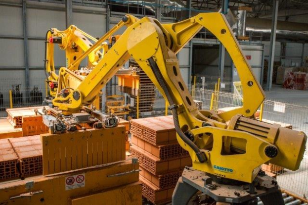 Ein großes Lagerhaus voller numerous boxes, Kräne und Industriegeräte, mit einem Zaun und Pfählen im Vordergrund und einer Wand im Hintergrund.