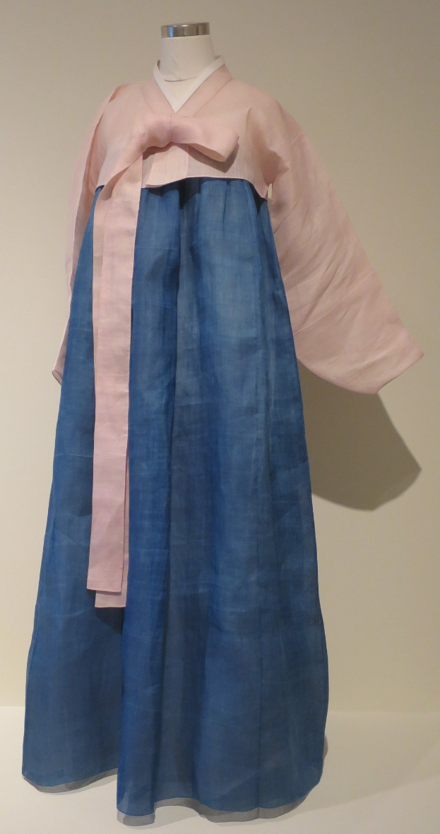 Eine Schaufensterpuppe in einem blauen und pinken Hanbok, einem traditionellen koreanischen Kleid, das in einem Museum mit einem neutralen Hintergrund präsentiert wird.